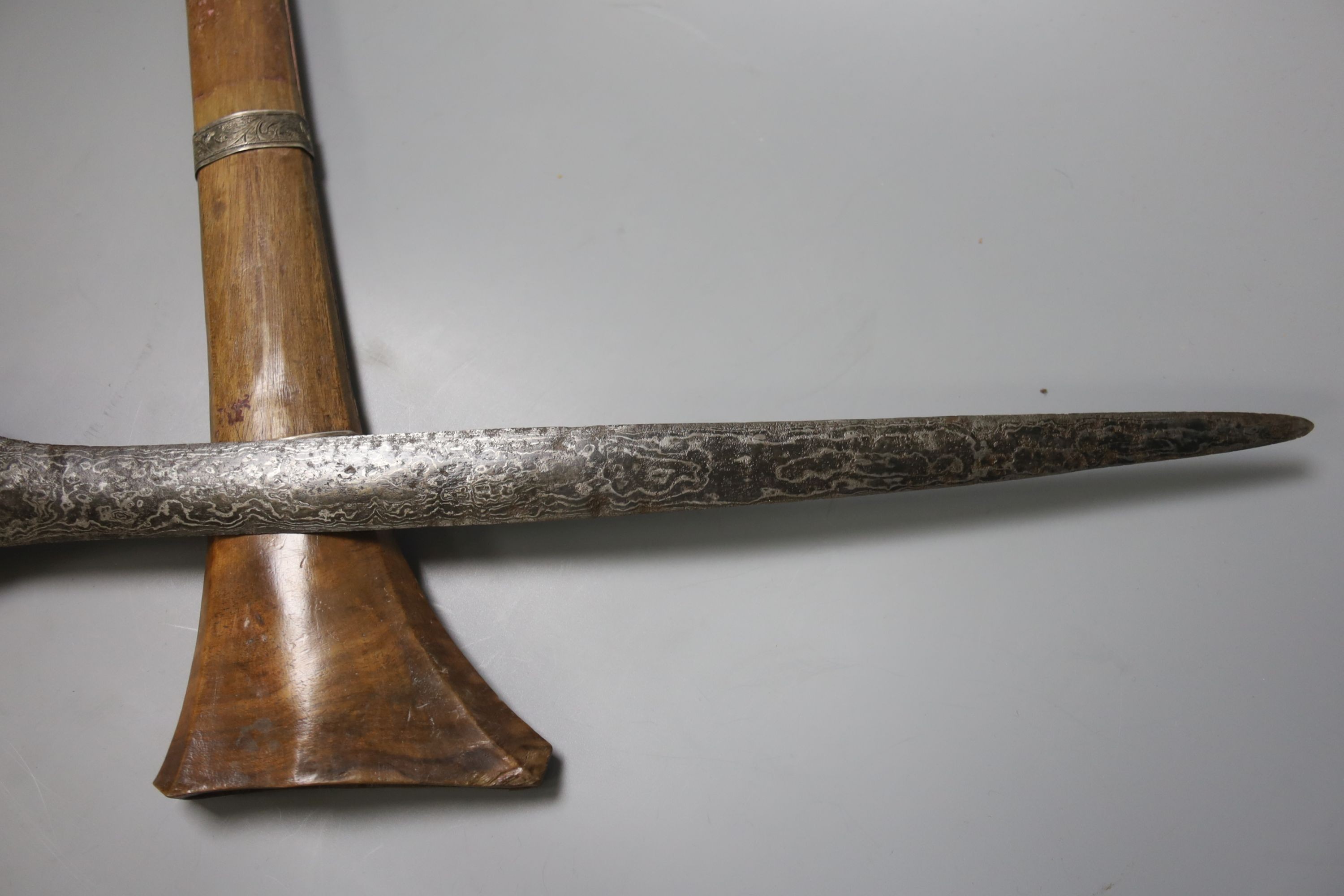 An Indonesian dagger kris, 19th century, earlier broad black and silver-coloured watered blade, brass mounted handle wound with woven hair, wooden scabbard with engraved silver mounts, blade 43.5cms